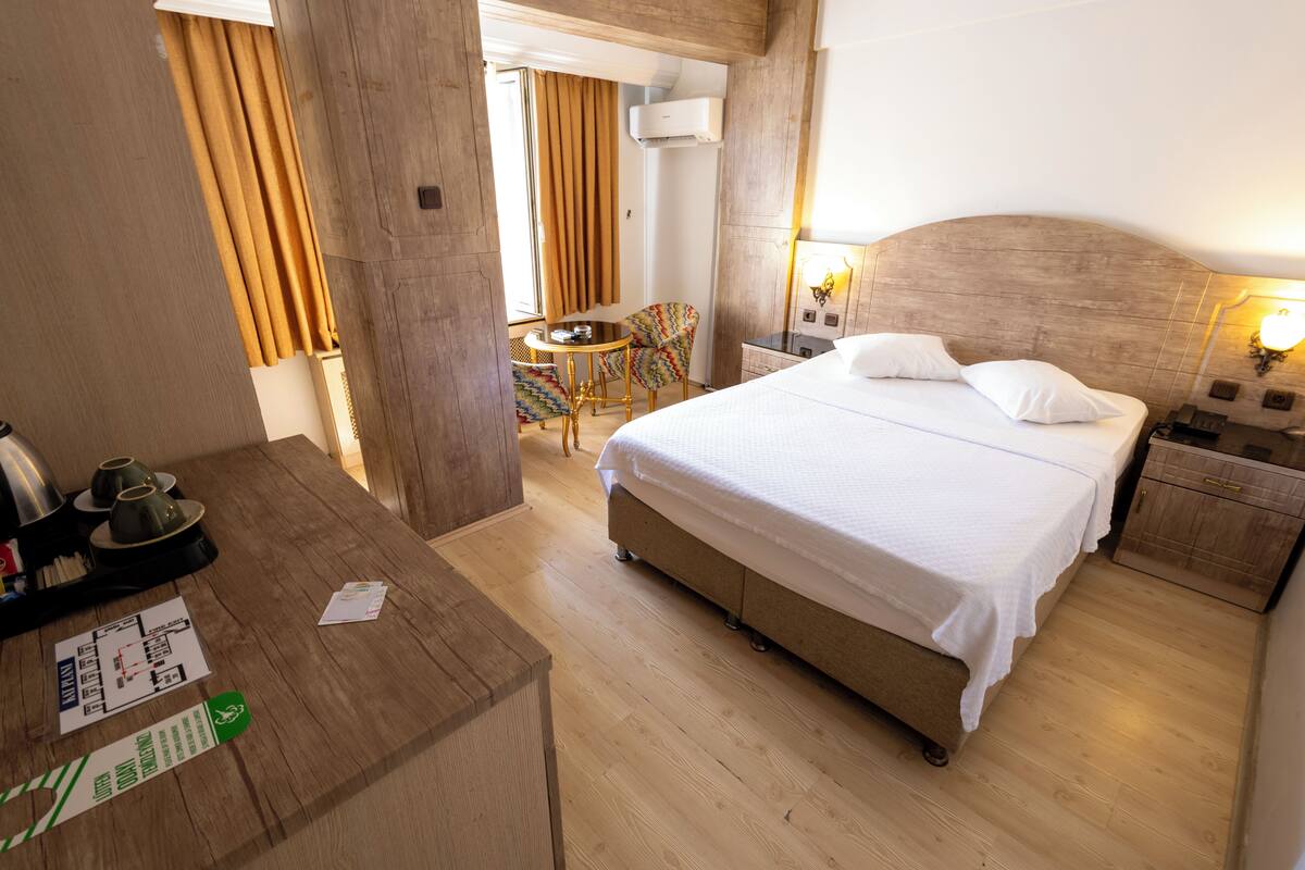 A hotel room with a wooden floor, a bed with white bedding, a nightstand, a desk with a chair, and a small table with a chair.