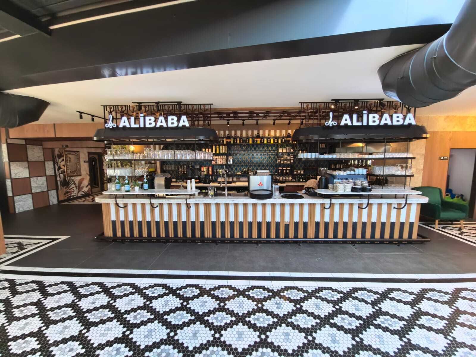 Zona de bar con dos letreros de Alibaba, una barra con varios artículos y un suelo con diseño.
