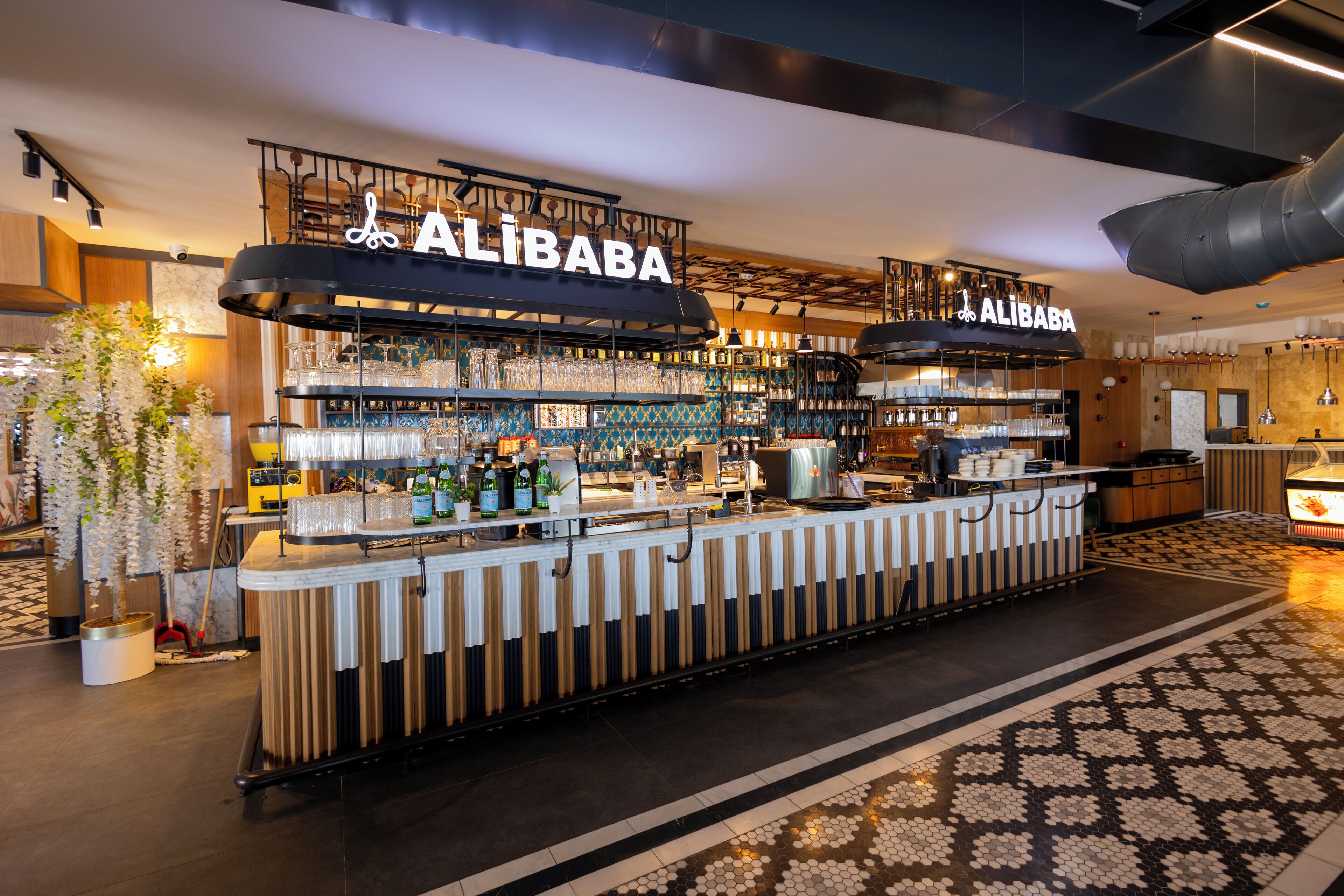 Zona de bar con letrero 'ALIBABA', estantes con botellas, vasos y una barra.