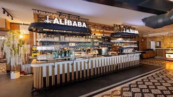 Zona de bar con letrero 'ALIBABA', estantes con botellas, vasos y una barra.