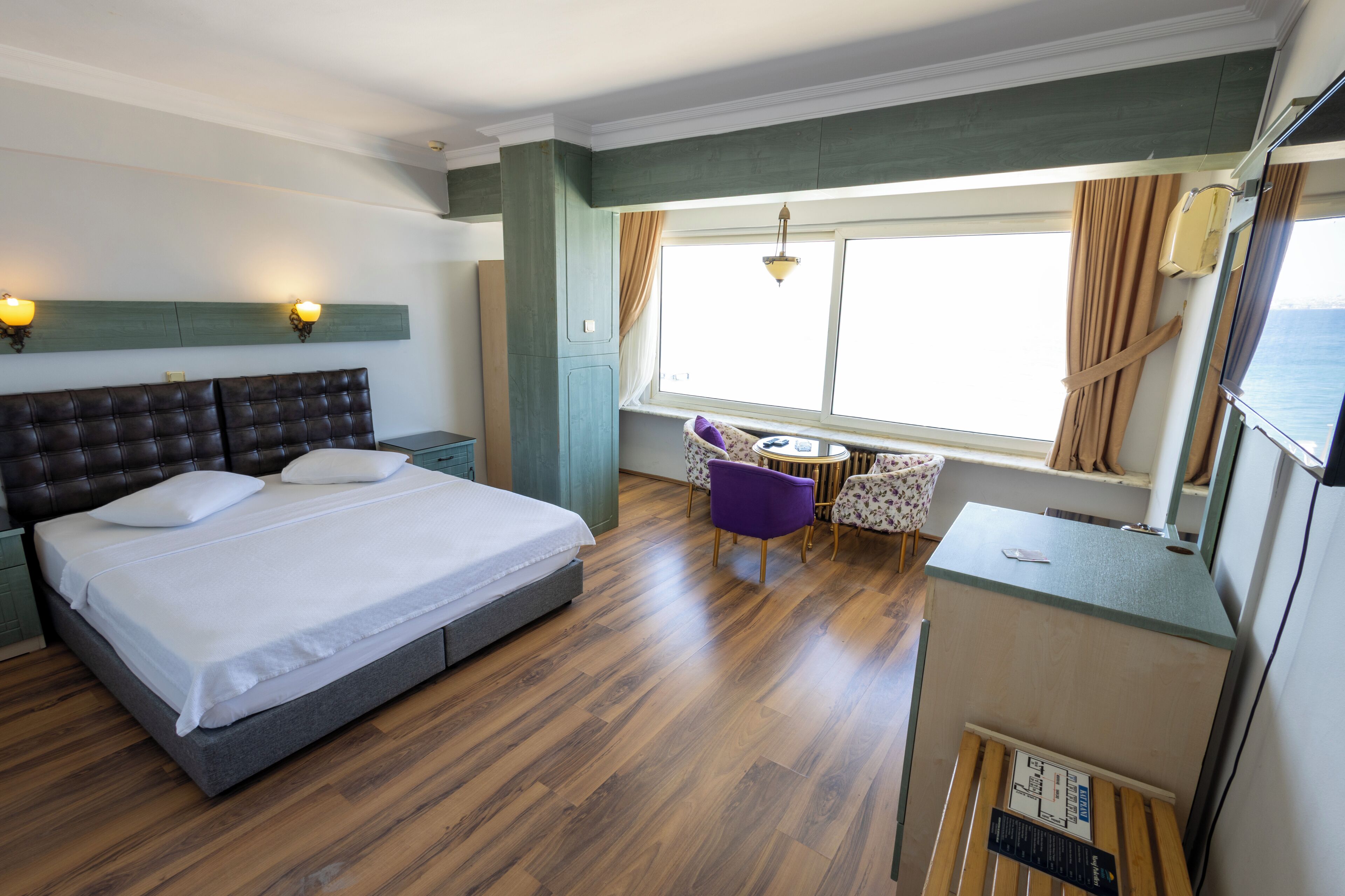 Ein Hotelzimmer mit Bett, Schreibtisch, Stuhl, einem kleinen Tisch und einem Fenster mit Vorhängen.