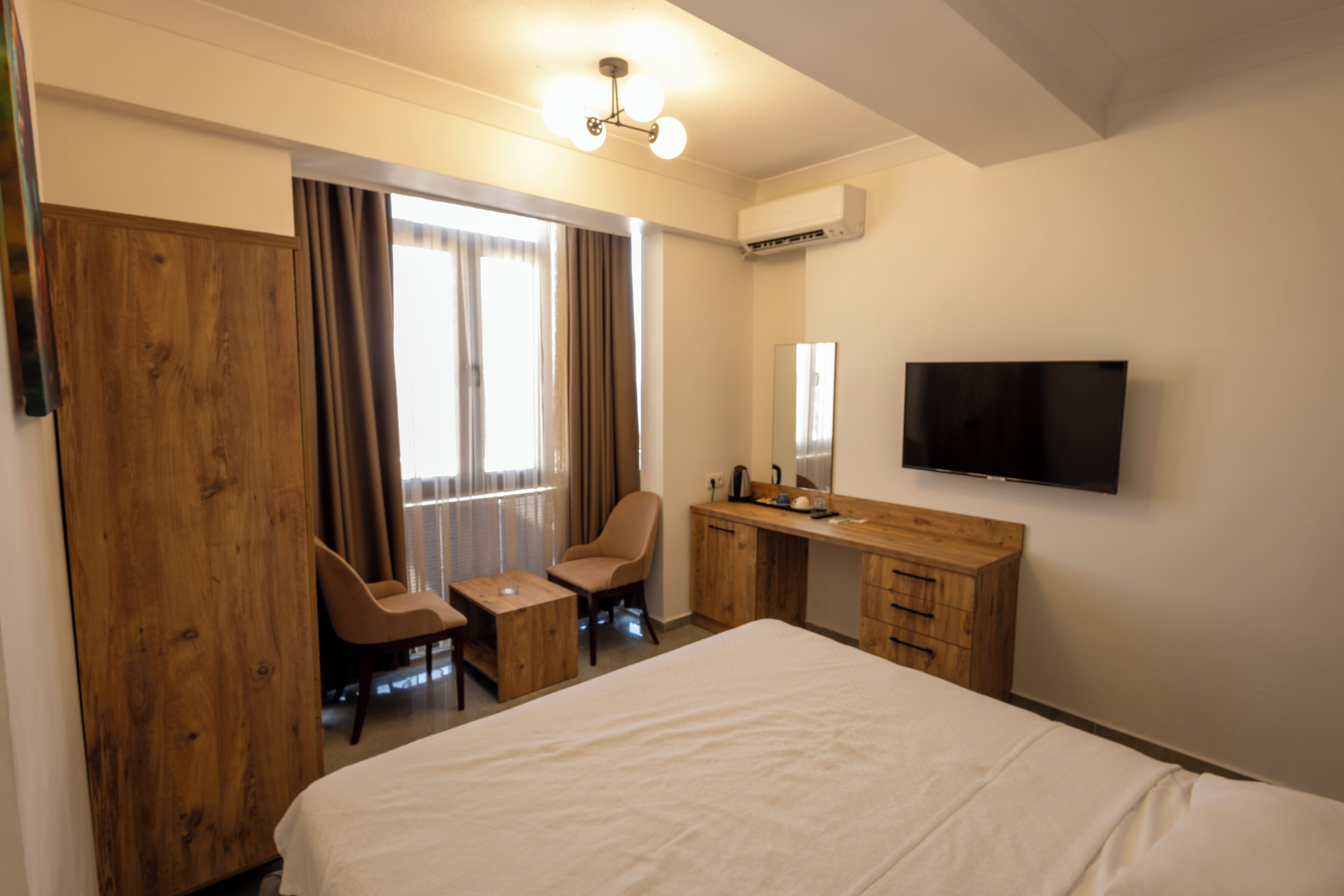 A hotel room with a large bed, a wooden desk, a chair, a television, and a window with curtains.