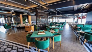 Un restaurante moderno con sillas tapizadas en verde, mesas de madera y un suelo estampado.