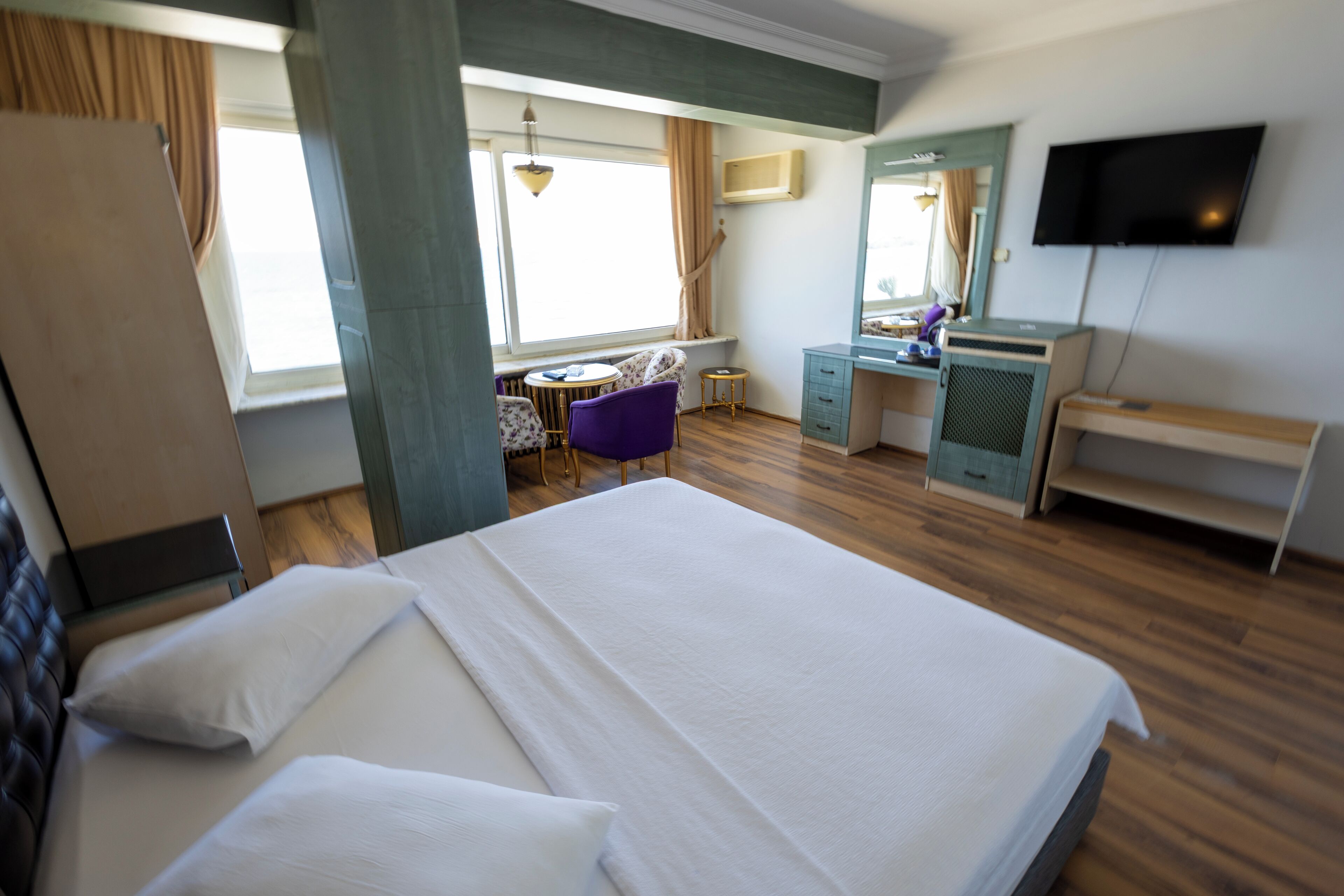 Una habitación de hotel con una cama grande, un escritorio, una silla, un televisor y una ventana con cortinas.