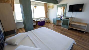 Una habitación de hotel con una cama grande, un escritorio, una silla, un televisor y una ventana con cortinas.