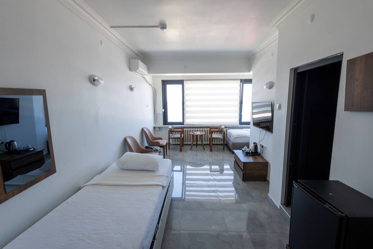 A hotel room with a bed, a desk, a chair, a TV, and a window with blinds.