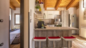 A modern kitchen with wooden beams, a central island with bar stools, and a microwave. - Alida penthouse in Alghero city centre, 4 bedrooms and 2 bathrooms for 8 people (Alghero)