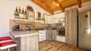 A modern kitchen with wooden ceiling beams, stainless steel appliances, and a central island with bar stools. - Alida penthouse in Alghero city centre, 4 bedrooms and 2 bathrooms for 8 people (Alghero)