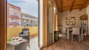 A balcony with wicker furniture, a dining table, and a view of neighboring buildings. - Alida penthouse in Alghero city centre, 4 bedrooms and 2 bathrooms for 8 people (Alghero)
