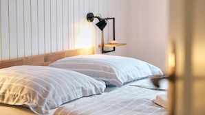 Una cama bien hecha con ropa de cama a rayas en una habitación con paneles de madera y una lámpara fijada a la pared.