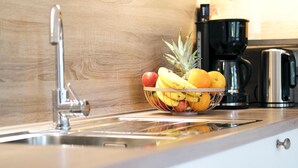 Una cocina con un lavaplatos de acero inoxidable, un frutero en la encimera y una cafetera.
