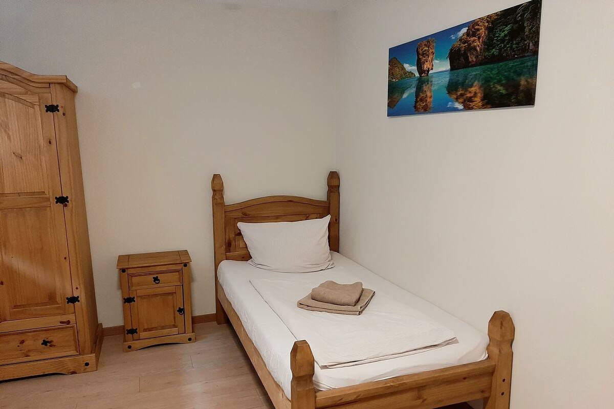 A bedroom with a wooden bed, a nightstand, a wooden wardrobe, and a wall-mounted picture.