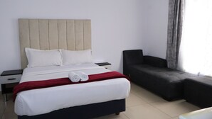 Ein Hotelzimmer mit Bett, Nachttisch, Sofa und einem Fenster mit Vorhängen.