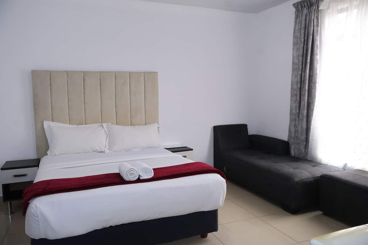 Une chambre d’hôtel avec un lit, une table de chevet, un canapé et une fenêtre avec des rideaux.