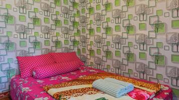 Un dormitorio con papel tapiz estampado, una cama con colcha floral y un cojín rojo con lunares.