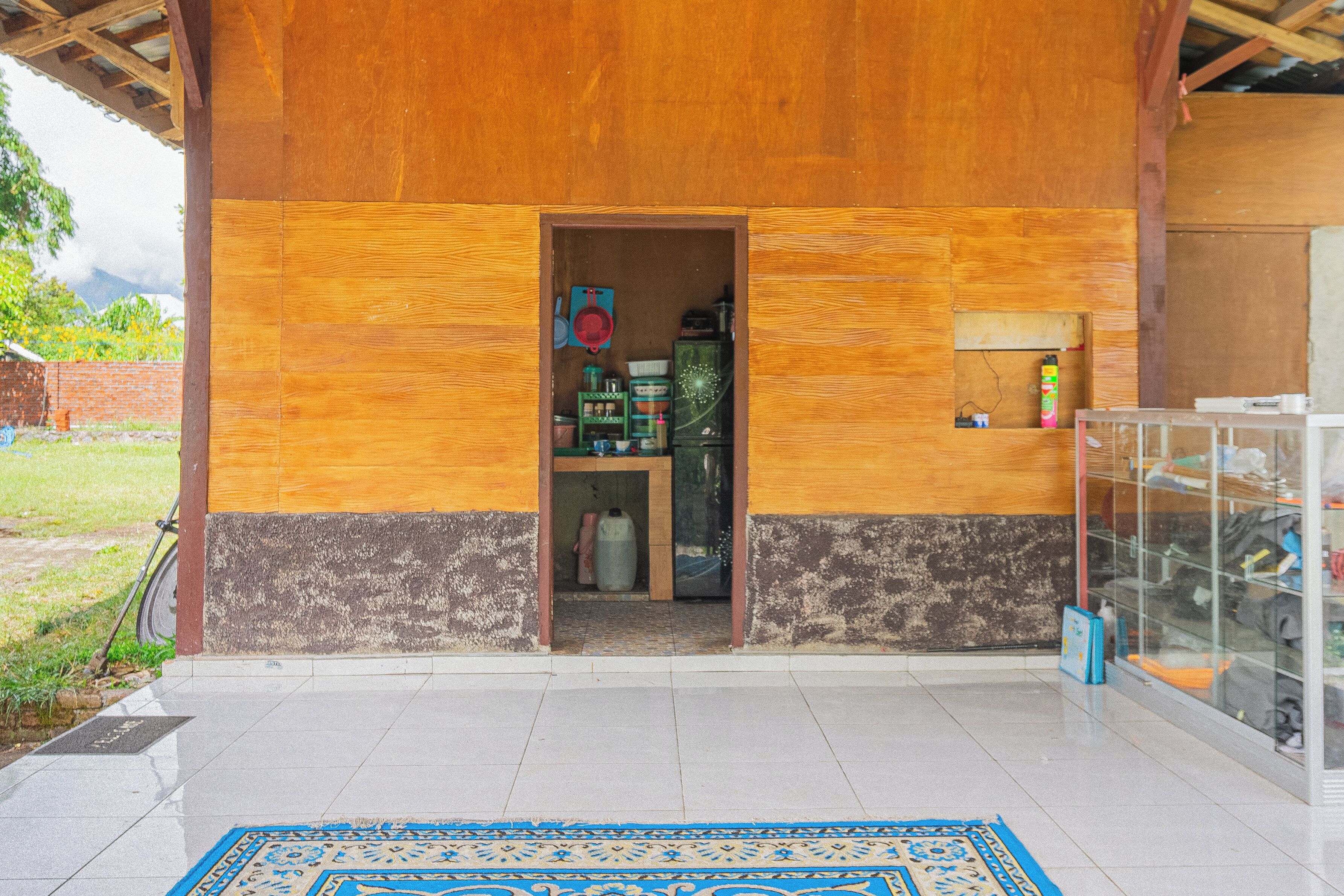 A wooden building with a tiled entrance and a blue patterned rug.