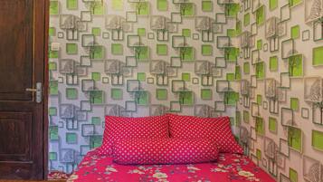 Um quarto com uma cama, porta de madeira e papel de parede estampado com formas geométricas e motivos de árvores.