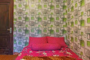 Um quarto com uma cama, porta de madeira e papel de parede estampado com formas geométricas e motivos de árvores.