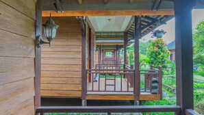 A wooden balcony with a railing, a hanging lantern, and a view of a garden with plants and a tree.