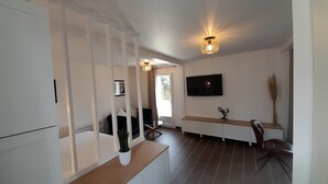 A modern living room with a TV, a wooden coffee table, a sofa, and a dining area with a table and chairs.