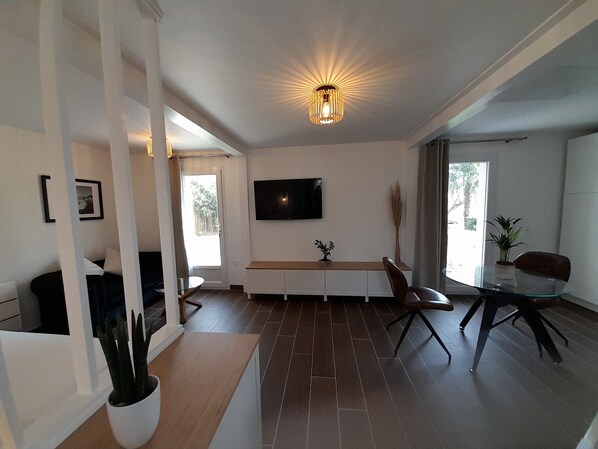 A modern living room with a flat-screen TV, a dining table, and a large window.