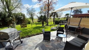 An outdoor patio with a grill, seating area, and a view of a grassy yard.