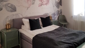 Un dormitorio con cama, mesita de noche, silla y un papel tapiz floral en la pared.