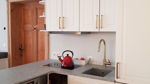 Una cocina con armarios blancos, un hervidor rojo, un fregadero y un horno empotrado.