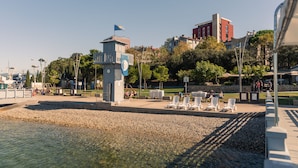 Un paseo marítimo con una pequeña torre, zonas de estar y un edificio al fondo.