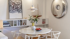 Un comedor moderno con una mesa redonda blanca, sillas blancas, un florero con plantas y un frutero.