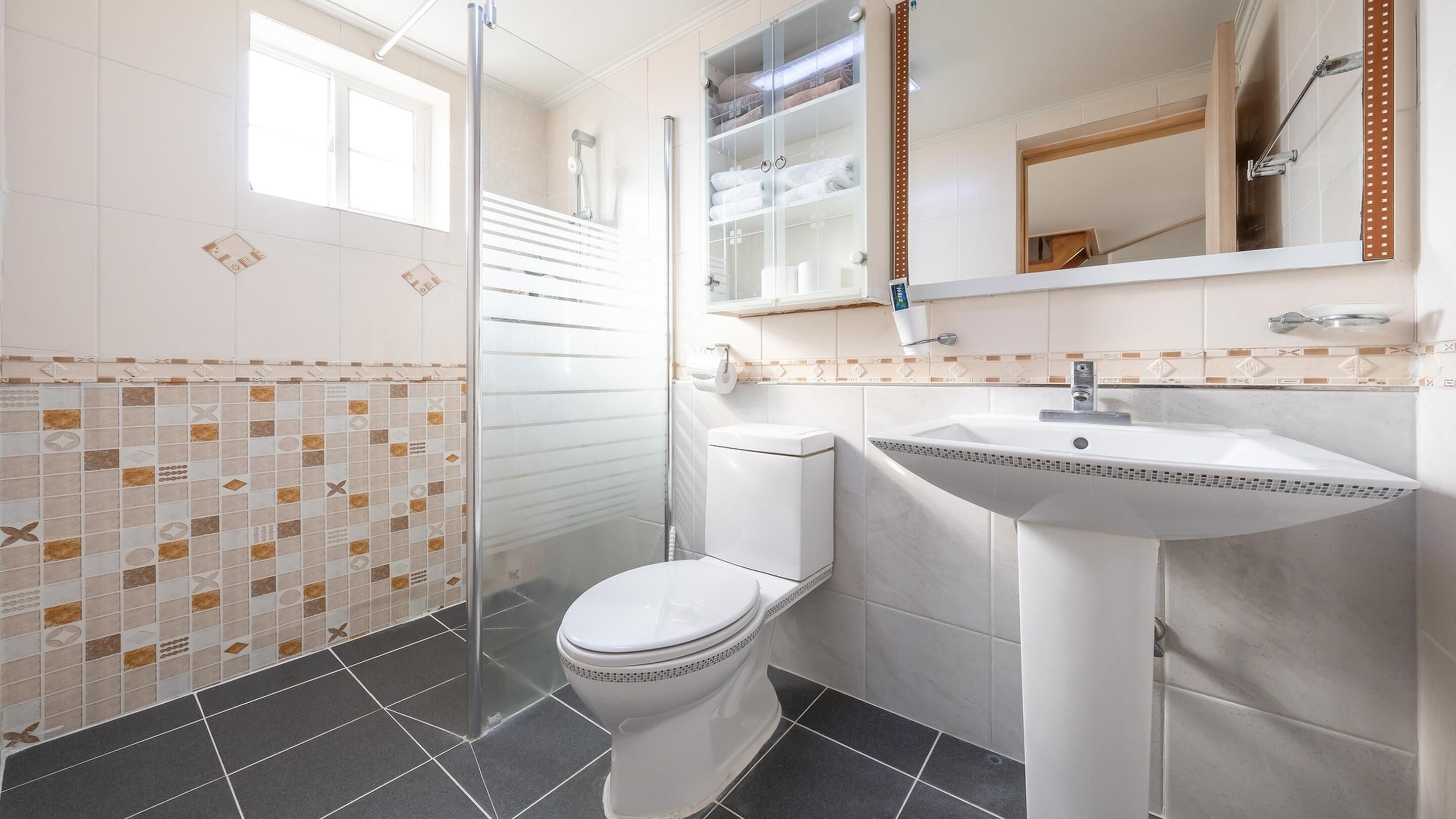 A modern bathroom with a glass shower enclosure, a white toilet, and a sink with a decorative tile backsplash.