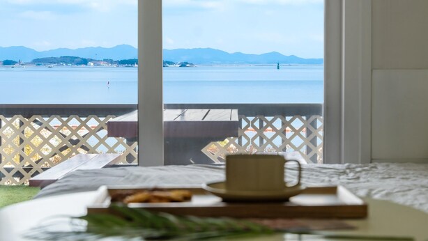 Un balcone con vista su un corpo d'acqua tranquillo e montagne in lontananza. Sul balcone c'è un vassoio con cibo e una tazza.