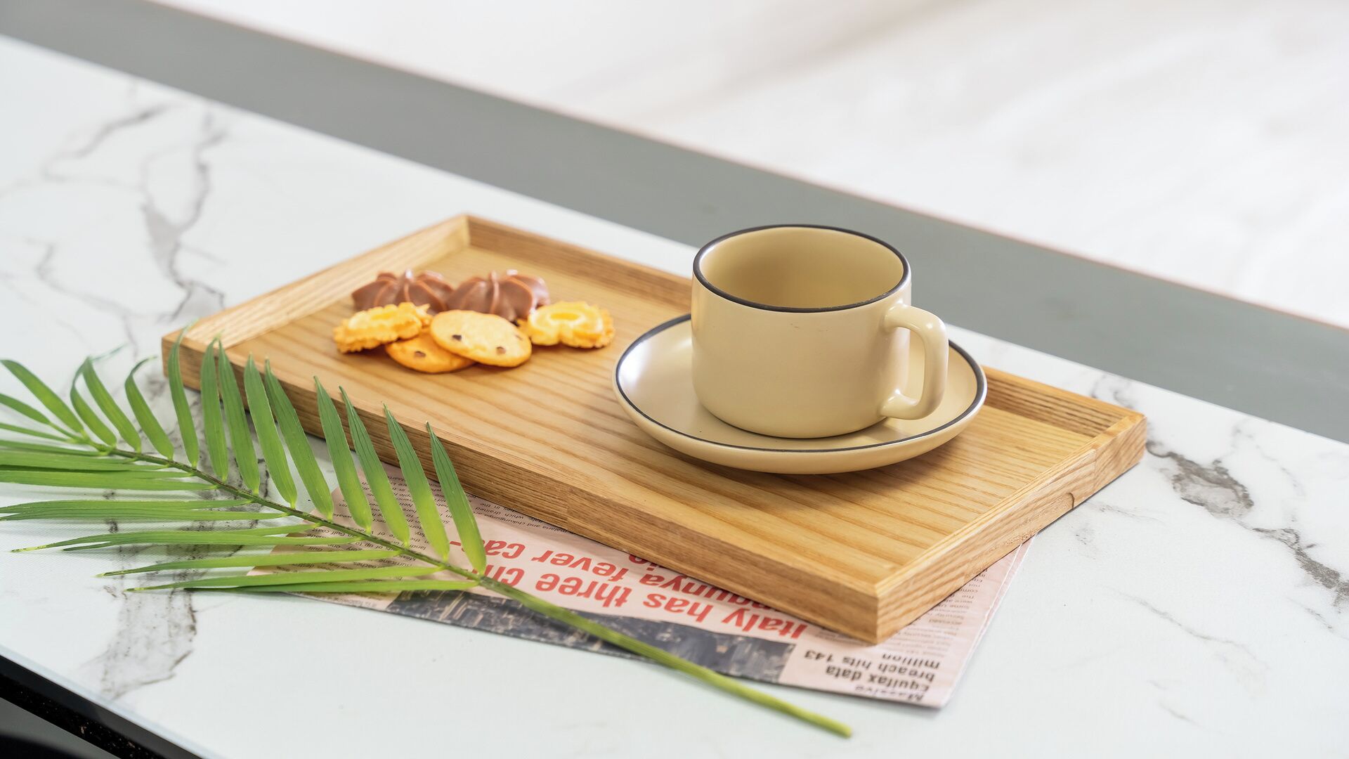 Una bandeja con una taza y galletas sobre una tabla de madera, colocada sobre una superficie de mármol con un periódico debajo.