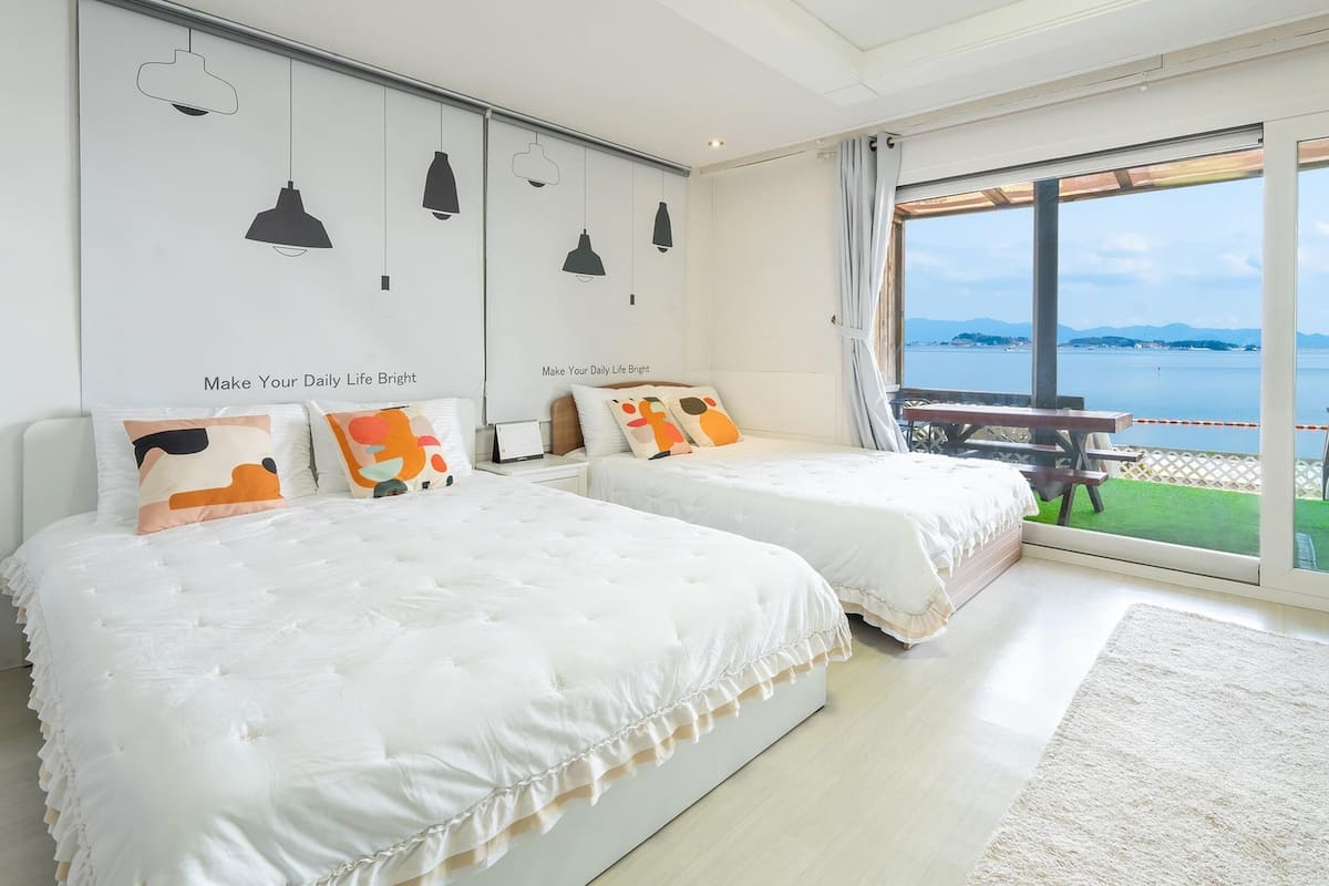 A bedroom with two beds, a large window with a view of the sea, and a balcony with a table and chairs.