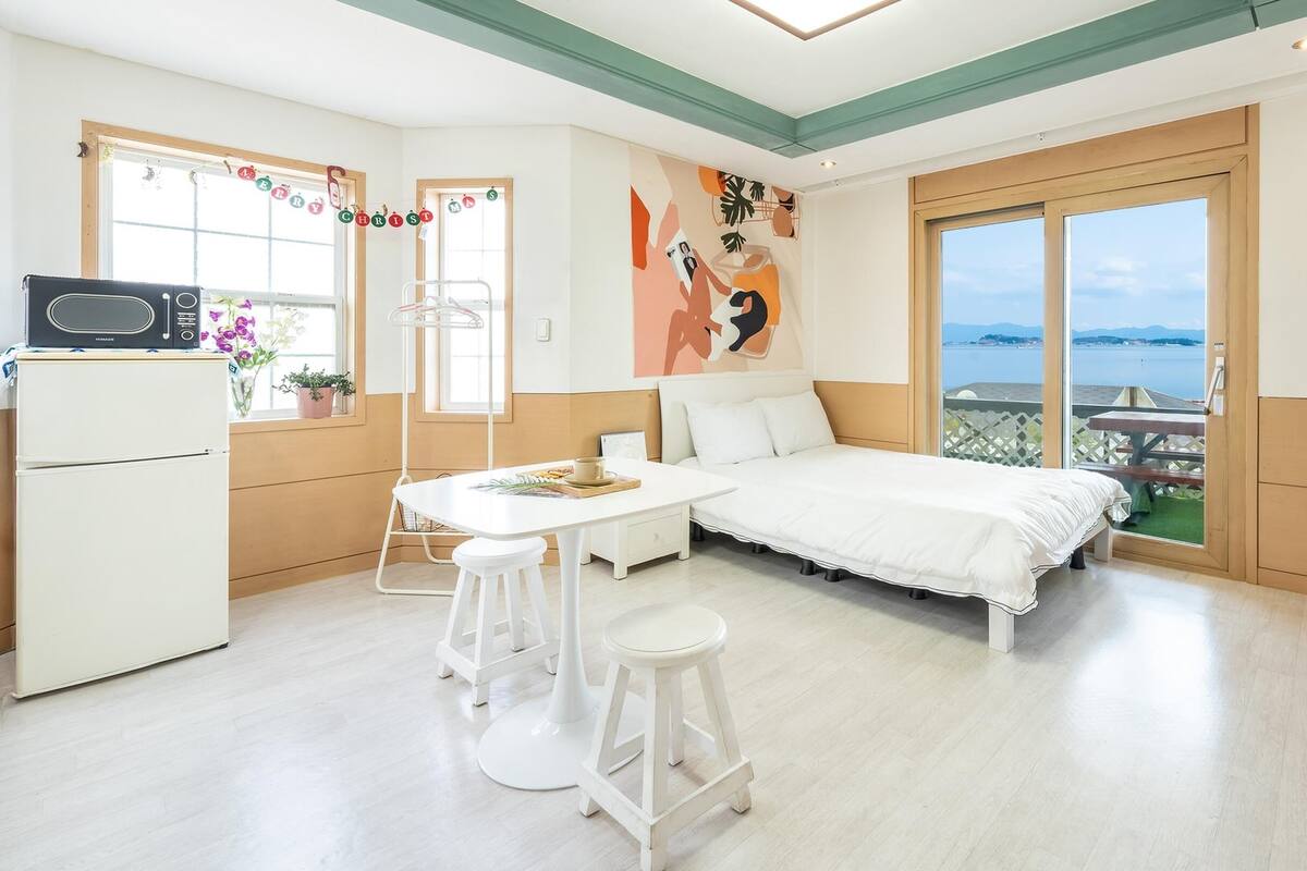 A modern room with a bed, a small kitchen area, and a balcony with a view.