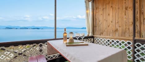 Una mesa dispuesta con una botella, vasos y un farol en un balcón con vista al mar.