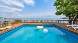 A swimming pool with a wooden deck, lounge chairs, and a view of the sea. - Taean Tteulapbada Pension (Taean)