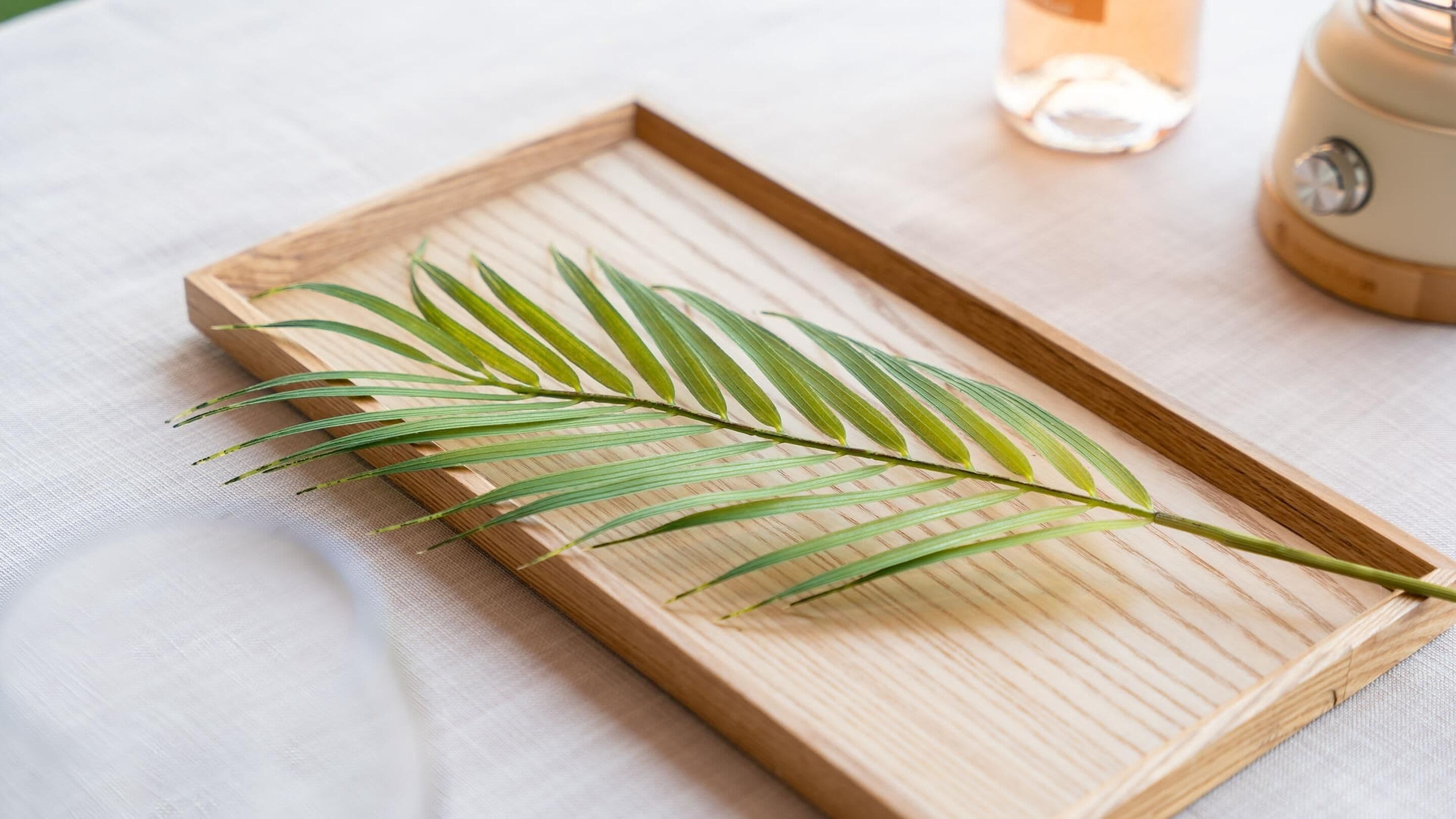 A wooden tray with a single palm leaf on a white fabric surface.