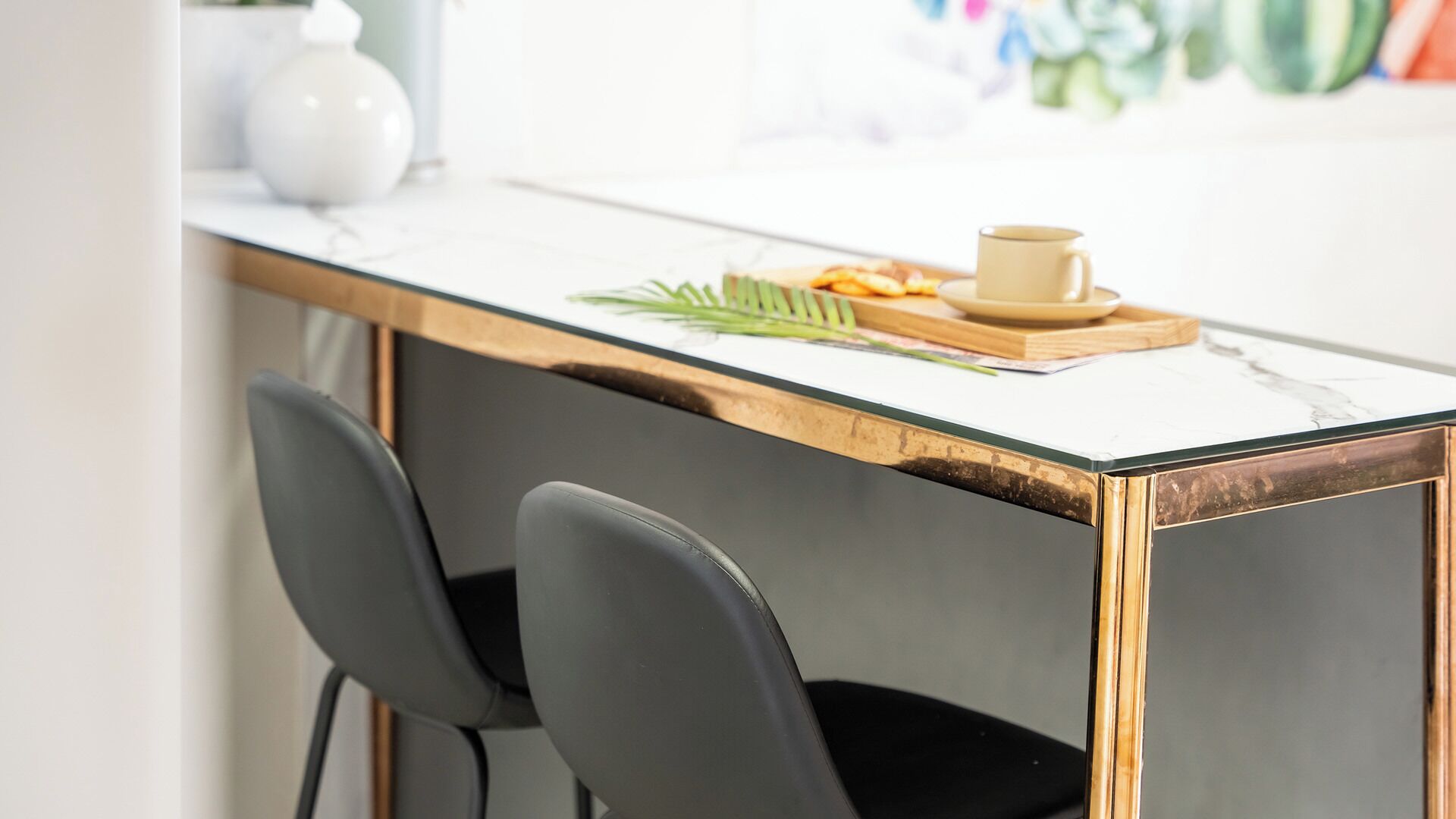 A modern kitchen with a marble countertop, two black chairs, and a small table with a cup and a plate of food.
