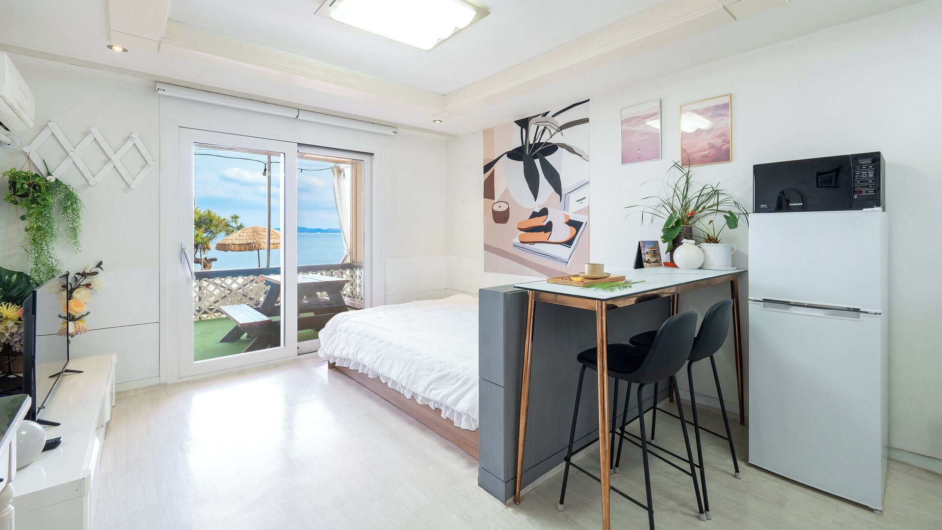 A modern bedroom with a balcony, a small kitchenette, and a view of the sea.