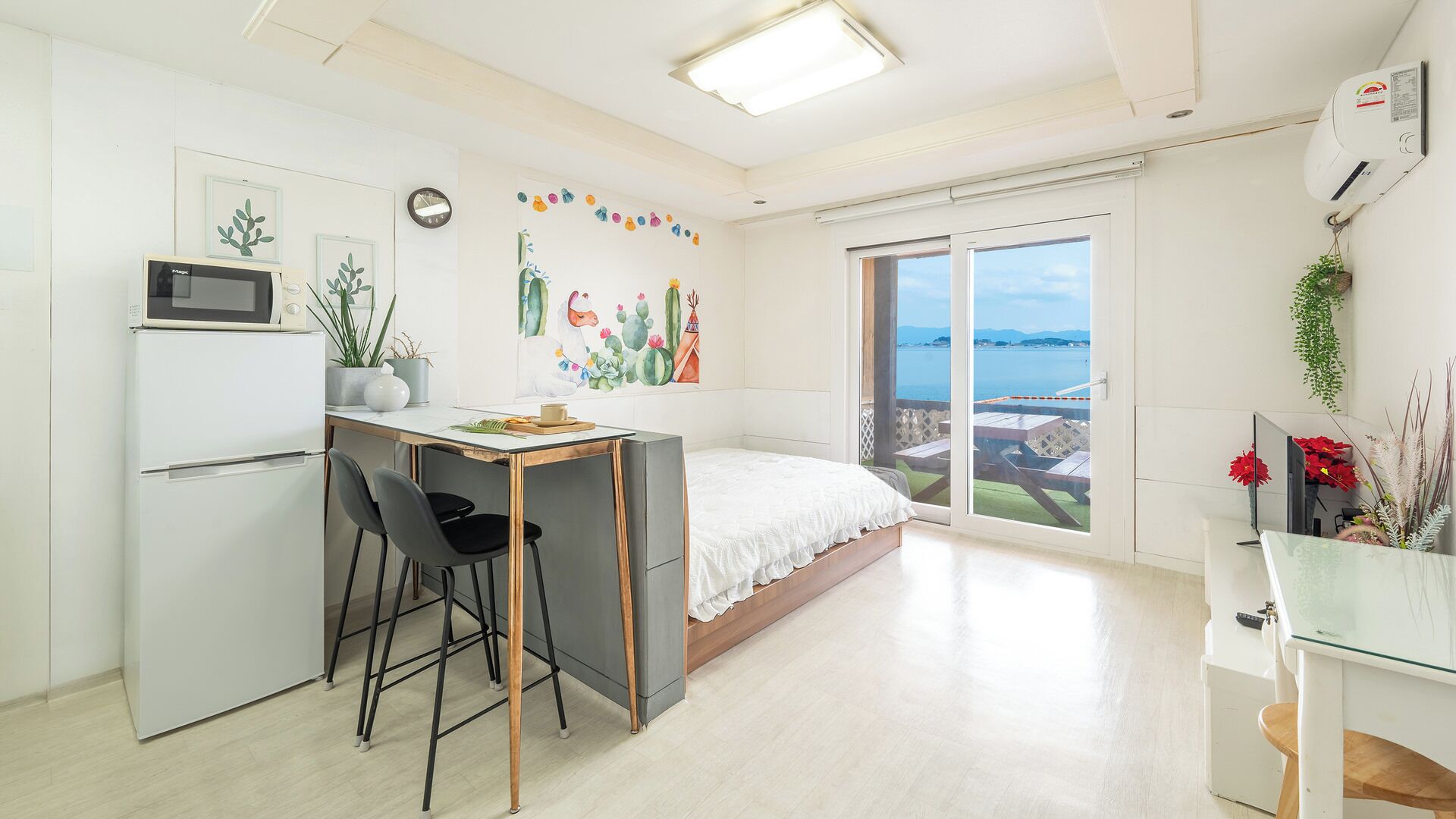 A compact room with a bed, a small kitchenette, a dining area, and a sliding glass door leading to a balcony with a view.
