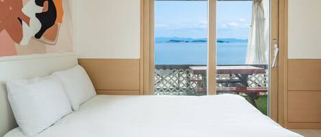 Un dormitorio con una cama grande, vista al mar y un patio con mesa y sillas.