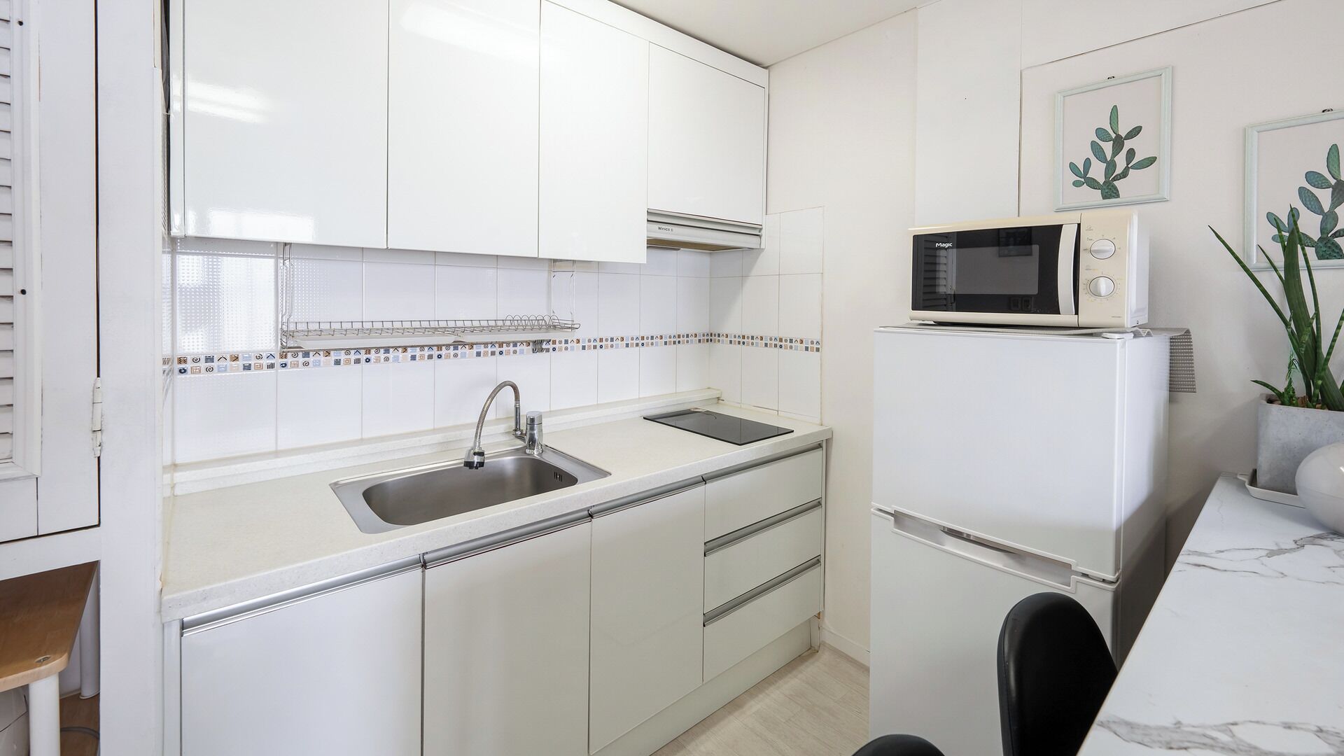 A kitchen with white cabinets, a stainless steel sink, a microwave, and a refrigerator.