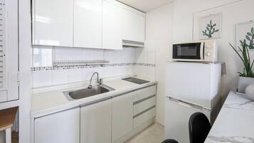 A kitchen with white cabinets, a stainless steel sink, a microwave, and a refrigerator.