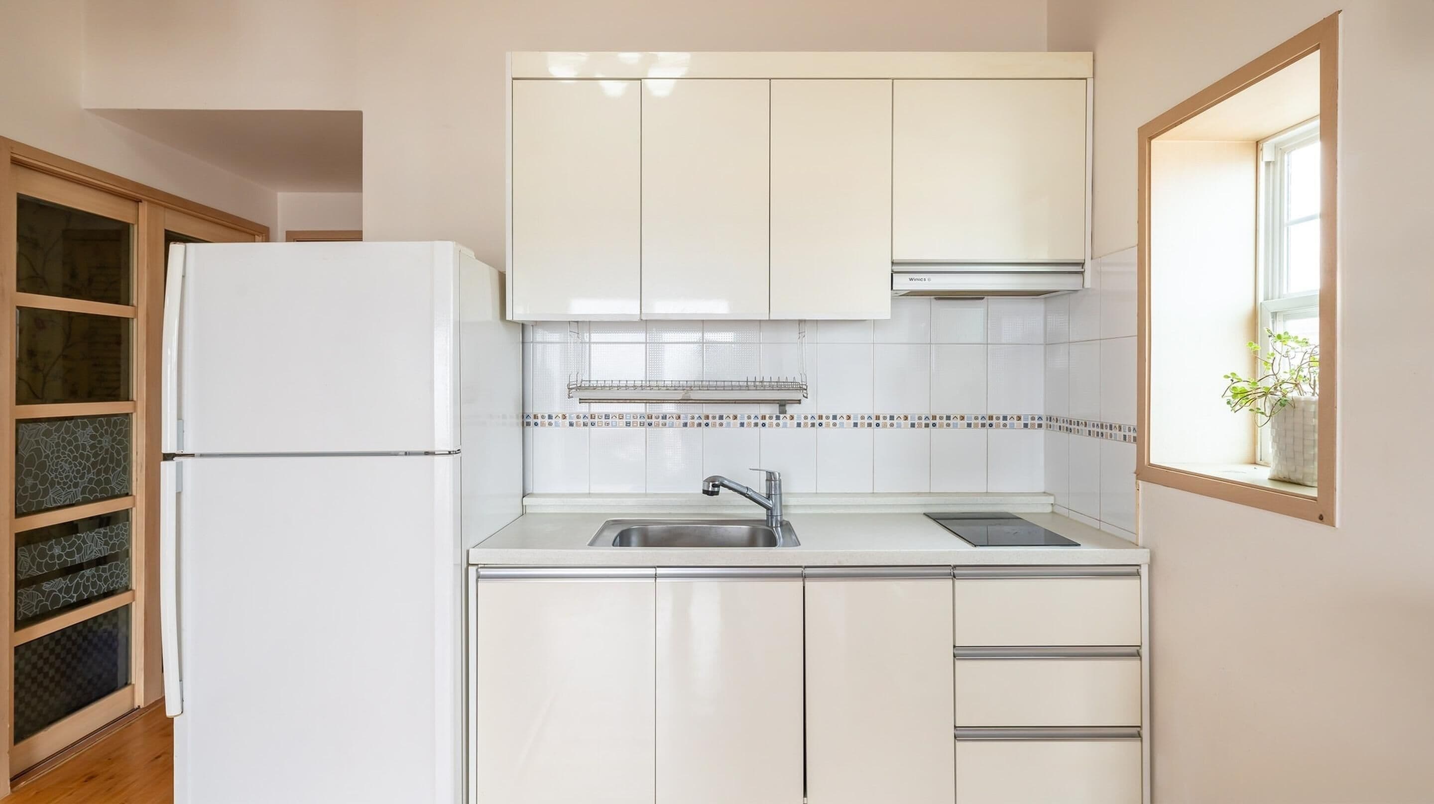 A compact kitchen with white cabinets, a stainless steel sink, and a window with a plant.