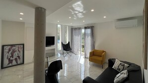 A modern living room with a flat-screen TV, a yellow armchair, a black sofa, and a glass coffee table. - Bas De Villa 60m² + Jardin au Golfe de Lava (Appietto)