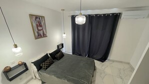 A bedroom with a bed, a bedside table, a wall-mounted TV, and a ceiling light fixture. - Bas De Villa 60m² + Jardin au Golfe de Lava (Appietto)