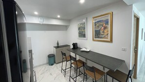 A compact kitchen with a dining area, featuring a marble floor, a long table with bar stools, and two framed pictures on the wall. - Bas De Villa 60m² + Jardin au Golfe de Lava (Appietto)