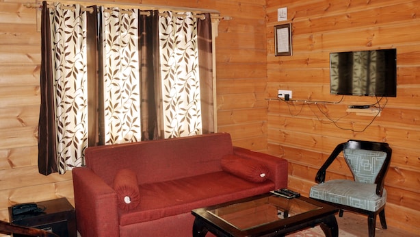 A wooden-paneled room with a red sofa, a patterned chair, a glass coffee table, a television mounted on the wall, and a framed picture above the TV. - Tip N Top (Lansdowne)