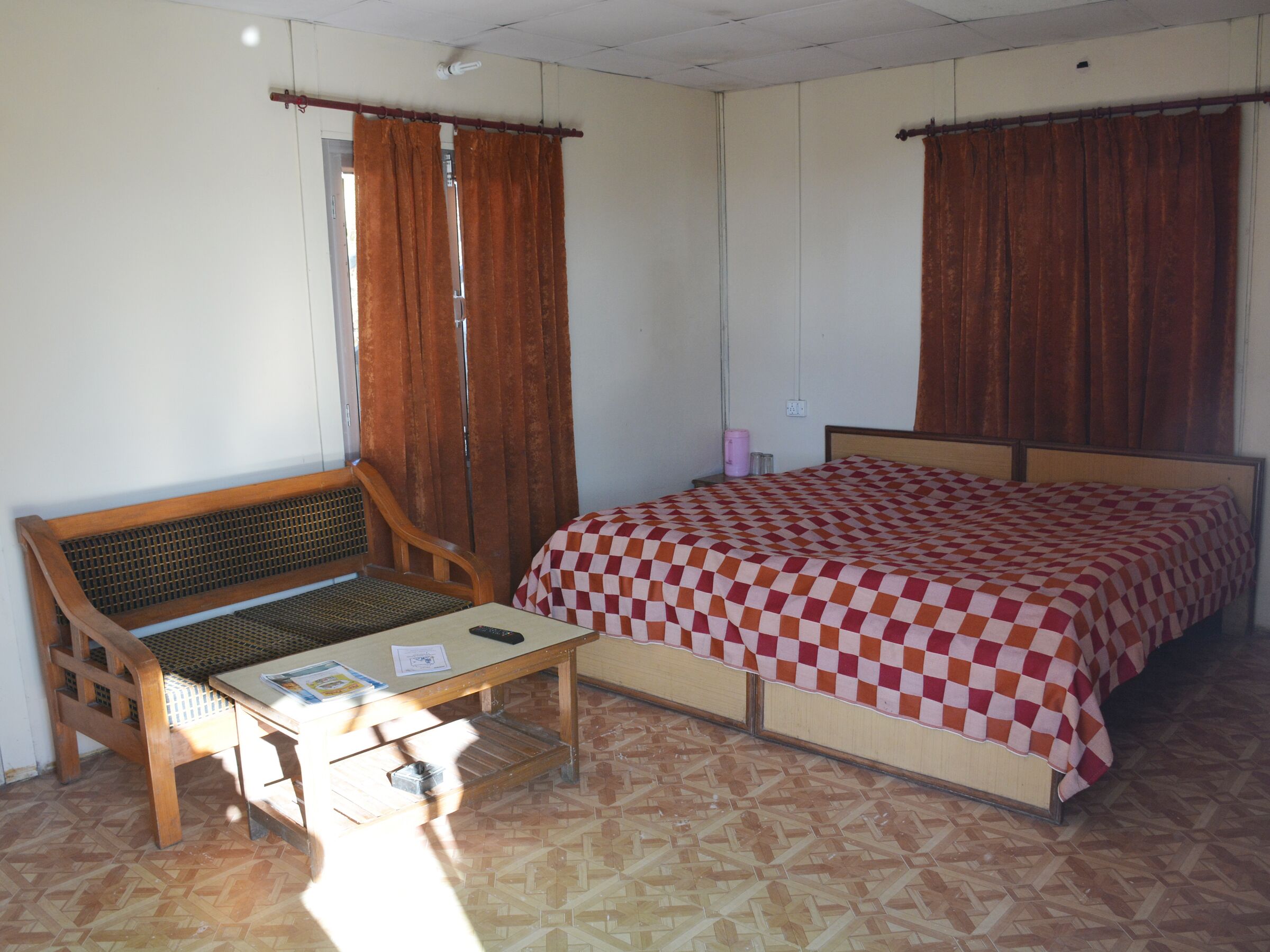 A room with a bed, a wooden bench, a small table, and a window with curtains.